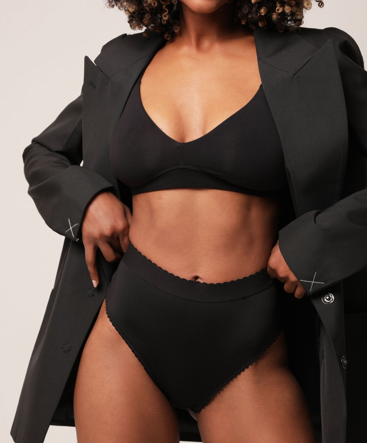 Avon abdominoplasty model wearing black lingerie with oversized blazer.