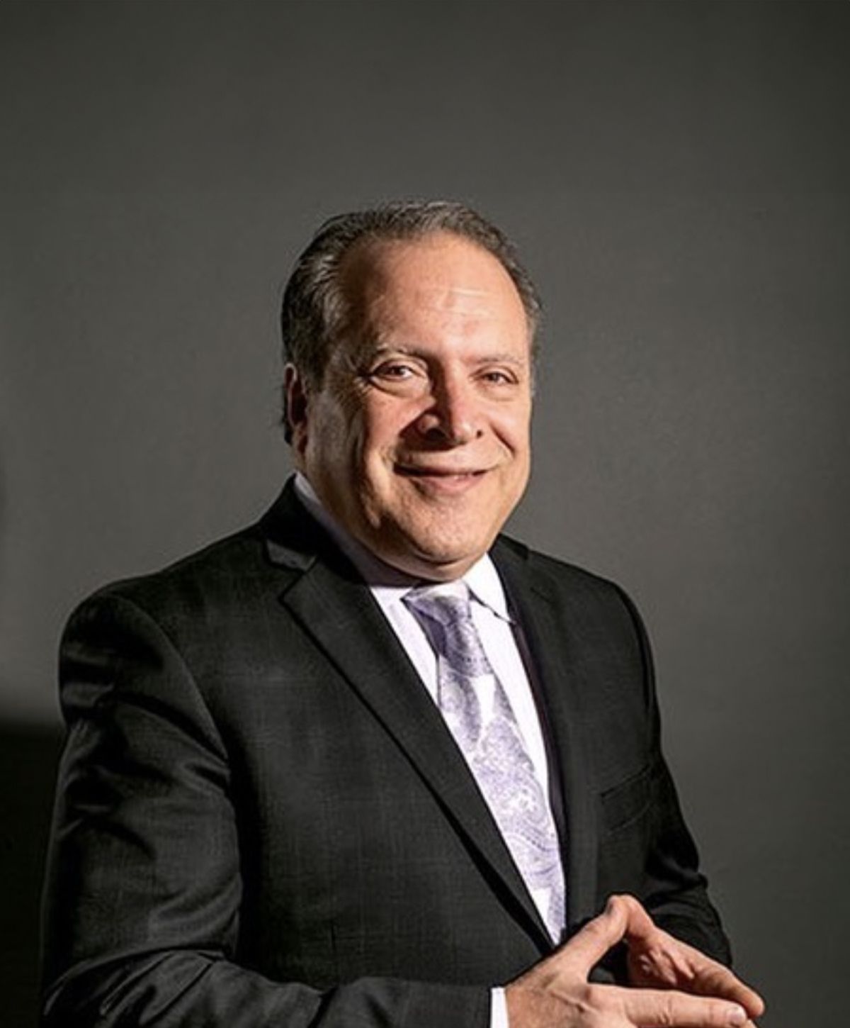 Avon plastic surgeon, Dr. Felice, in formal attire against dark background.