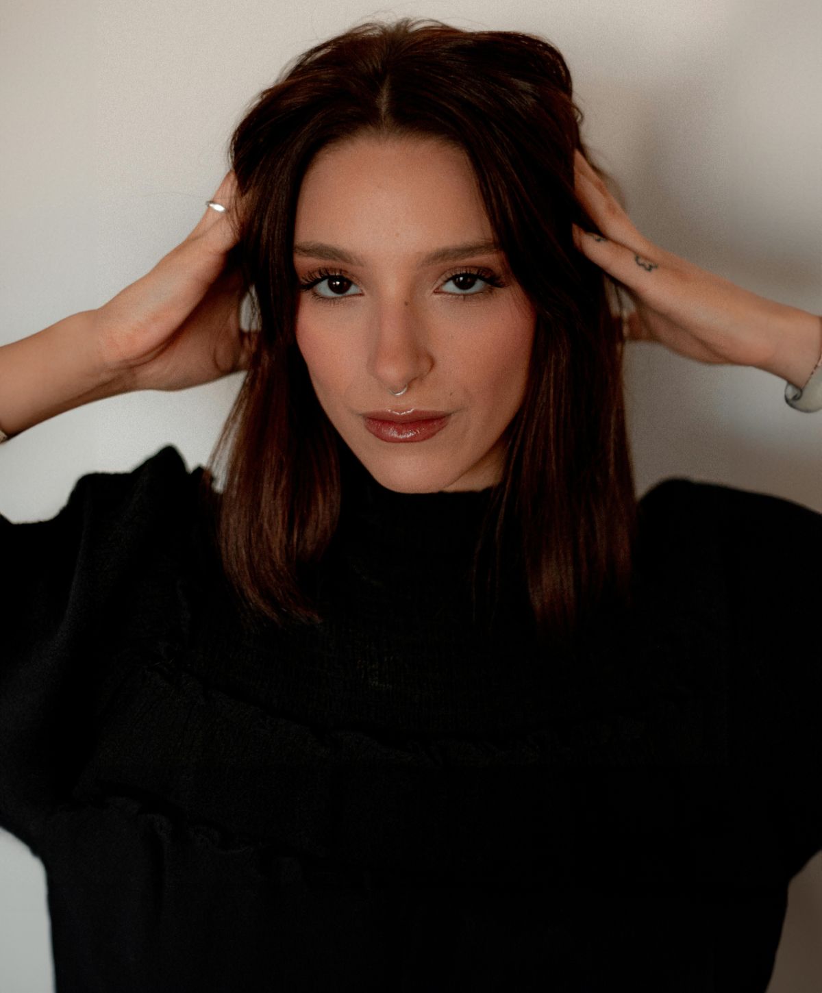 Farmington facial fat transfer model touching hair, wearing a black top.