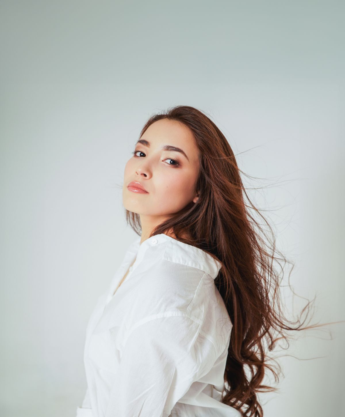Female hair restoration model with flowing hair in white blouse.