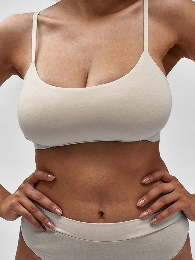 Avon nipple reduction model in casual beige lingerie, hands on hips.