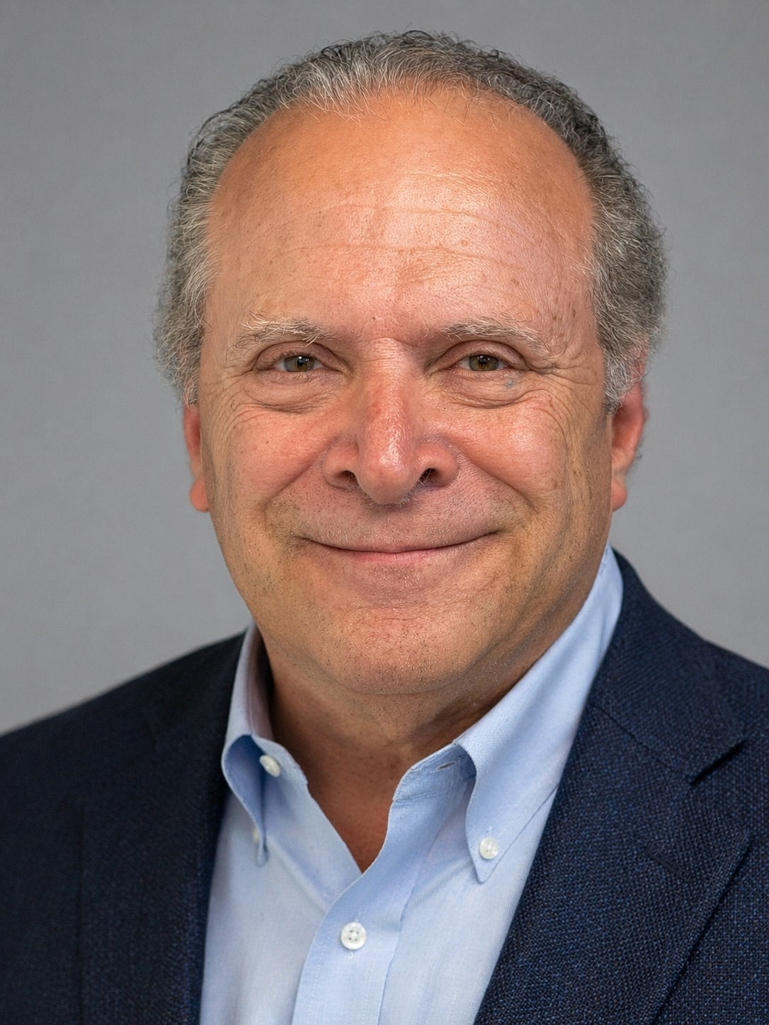 Smiling man in a blue suit, gray background.