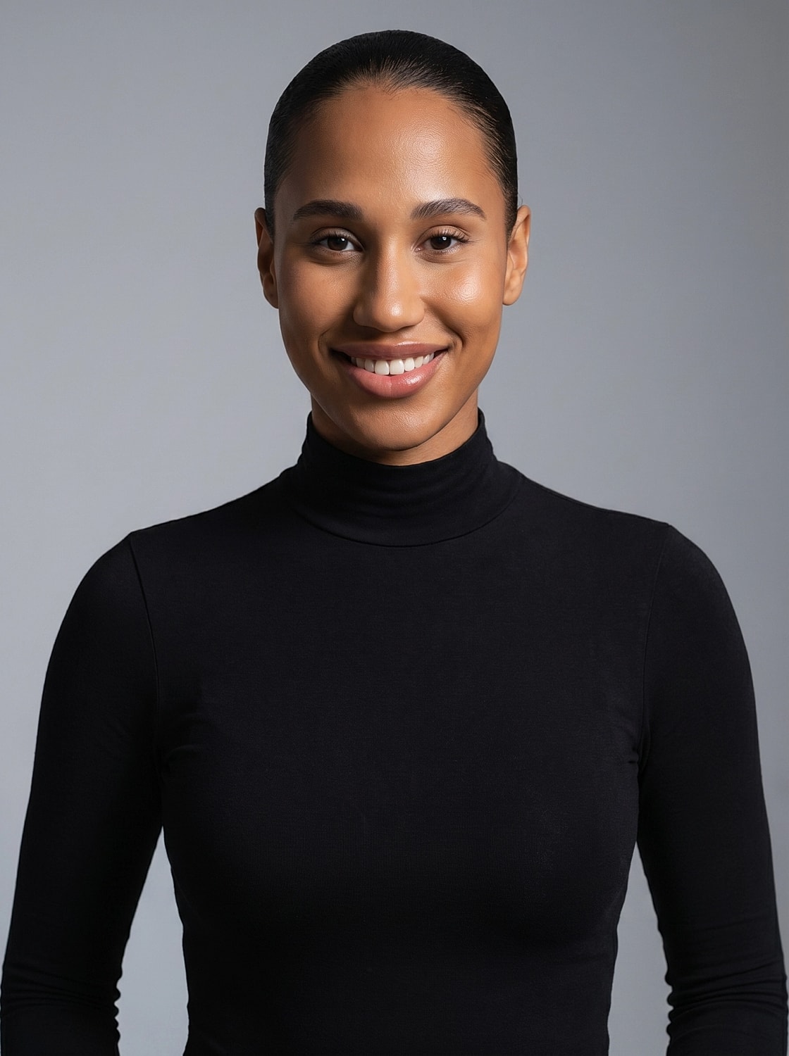 Smiling person in black turtleneck against gray background.