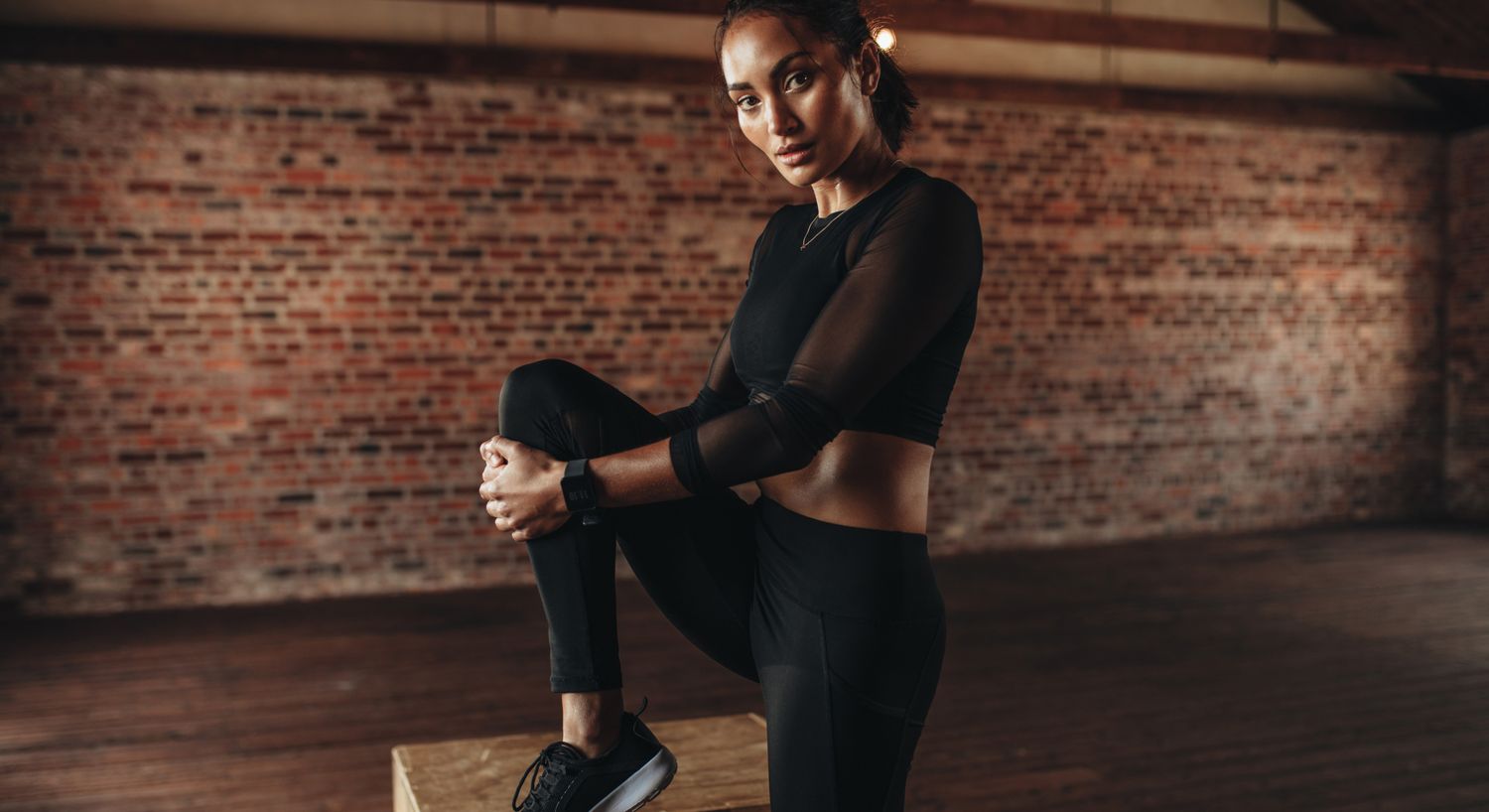 Woman stretching in athletic wear against brick wall.