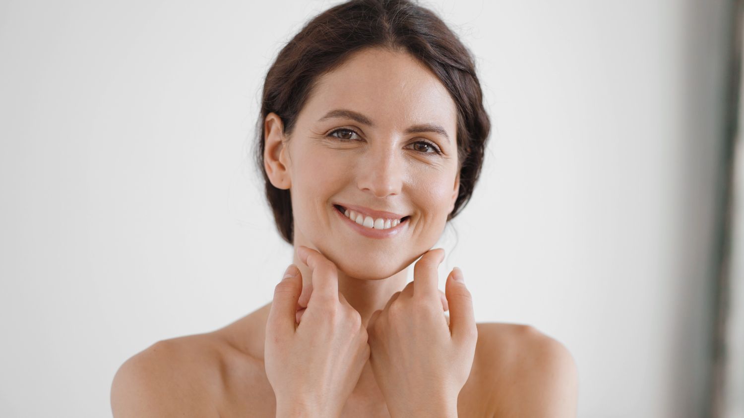 Woman smiling while applying skincare in mirror.