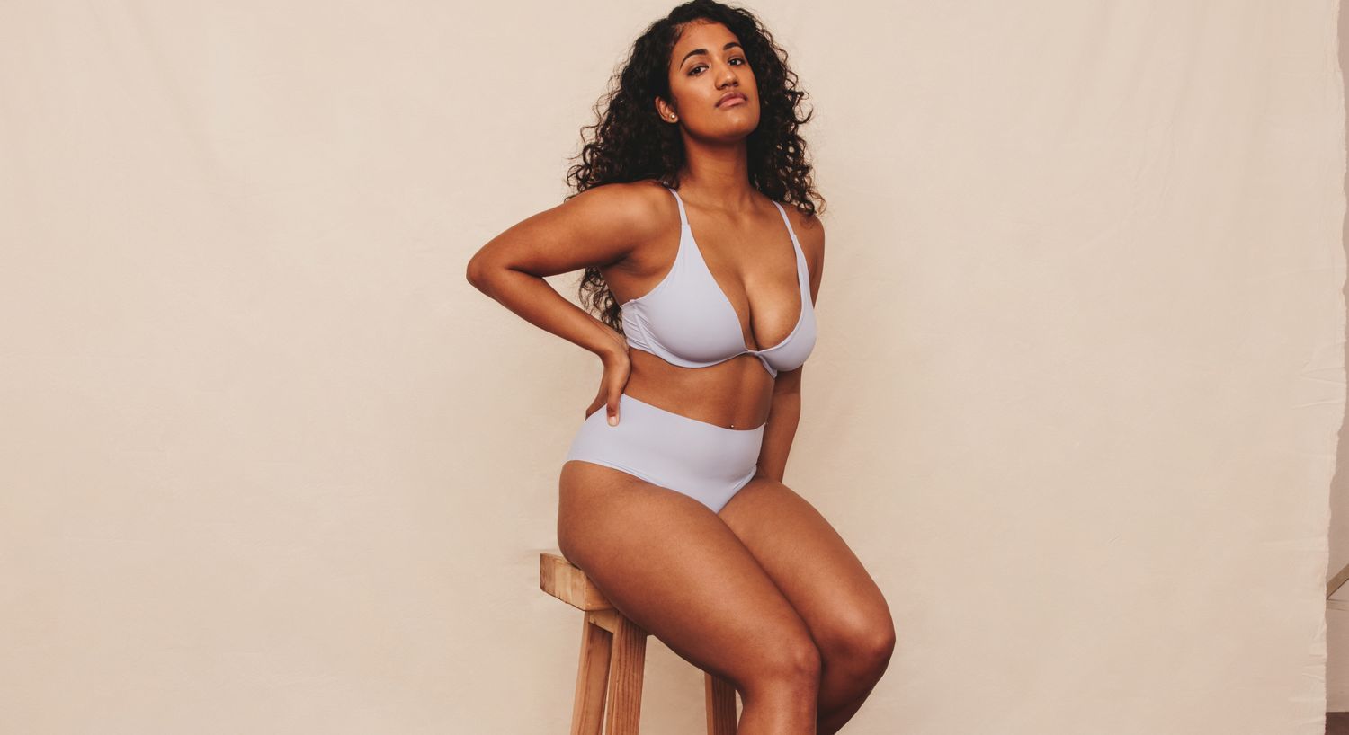 Model posing in light blue lingerie seated on stool.